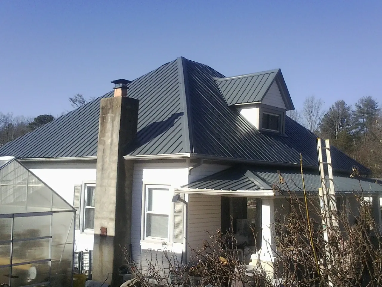 Dark blue standing seam metal roof on a white farmhouse with dormer — Slate & Tile Roof Repair by Roofing Brothers in Gillette