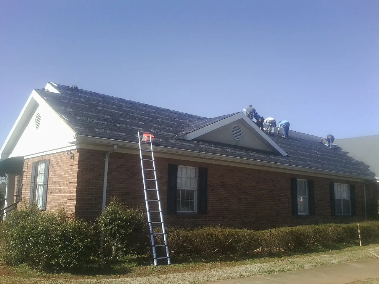 Crew tearing shingles off a brick ranch roof with a ladder set — Emergency Roof Repair work by our crew in Gillette