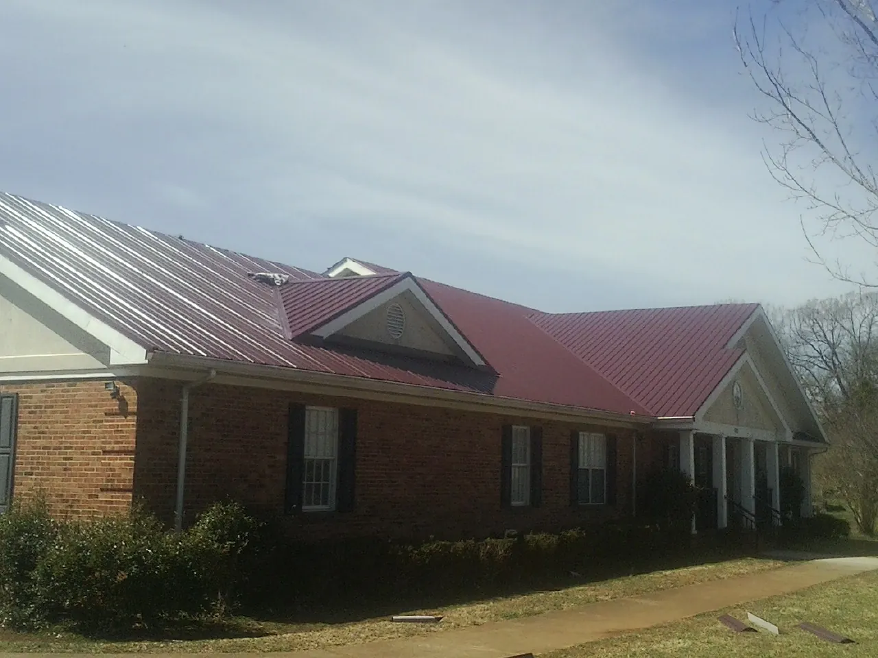 Red metal roof with gabled entries on a long brick building, from a Hail Damage Roof Repair job in Gillette