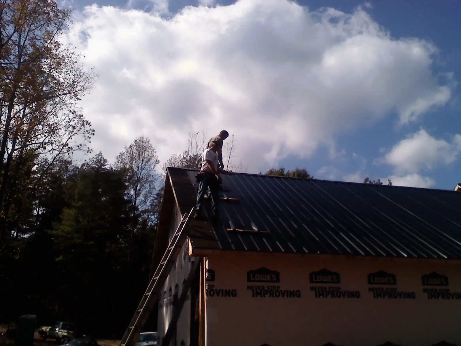 Roofer fastening dark metal panels high against a cloudy sky, from a Roof Inspection job in Gillette