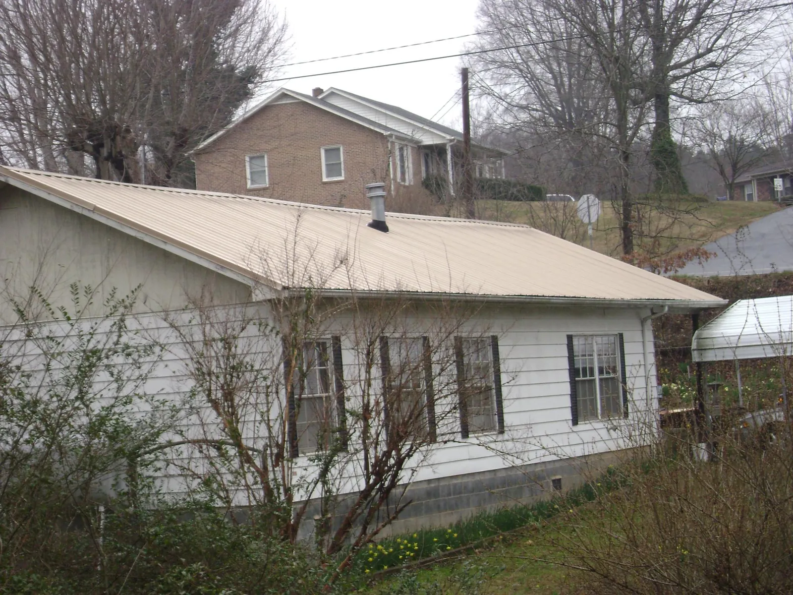 Tan metal roof on a white sided house set into a hillside — Commercial Roofing by Roofing Brothers in Gillette